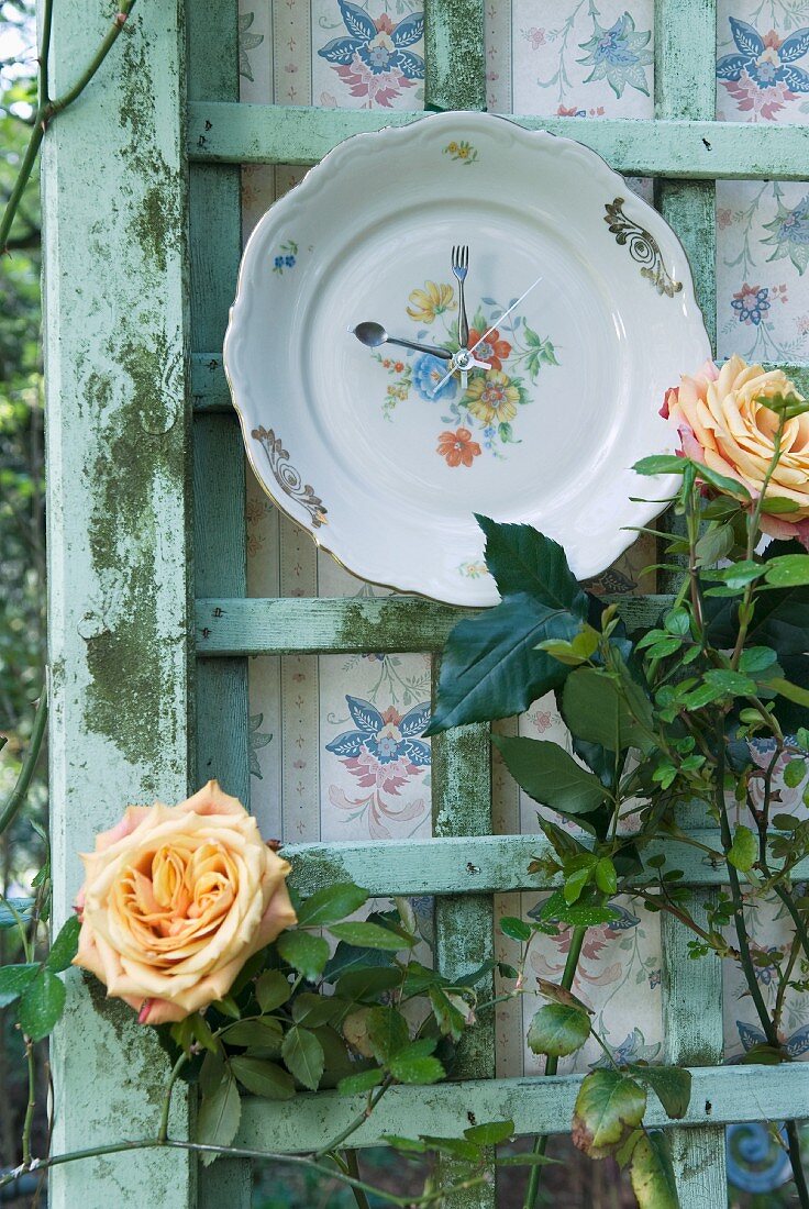 Old plate upcycled as clock on trellis with flowering rose