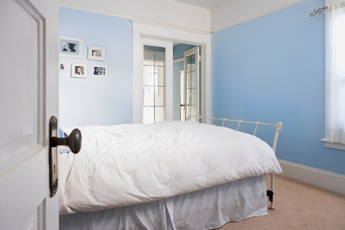 Bett mit weisser Bettwäsche in einem Schlafzimmer mit hellblauen Wänden