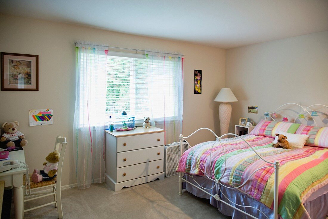 Doppelbett mit bunter Decke und weiße Kommode unter dem Fenster in einem Schlafzimmer