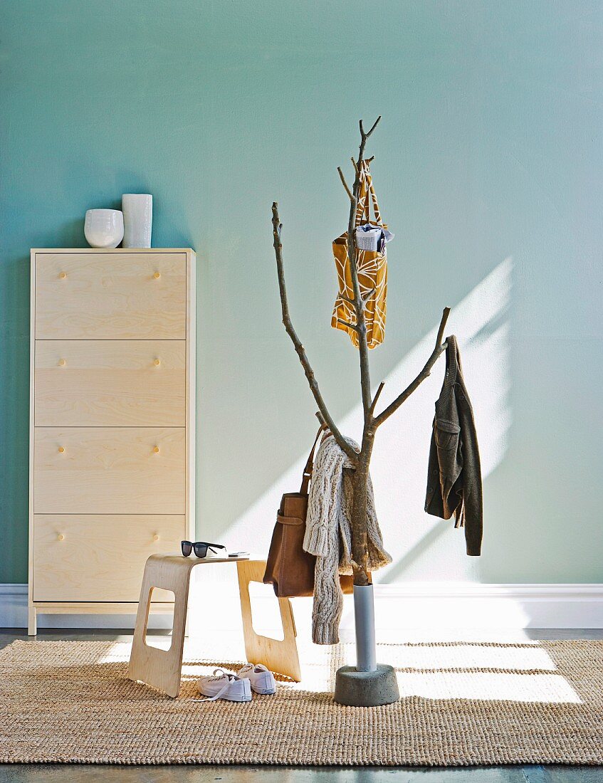 Lichtspiel auf stilisiertem Baum als Garderobe und moderner Hocker vor Schuhschrank an pastellblauer Wand