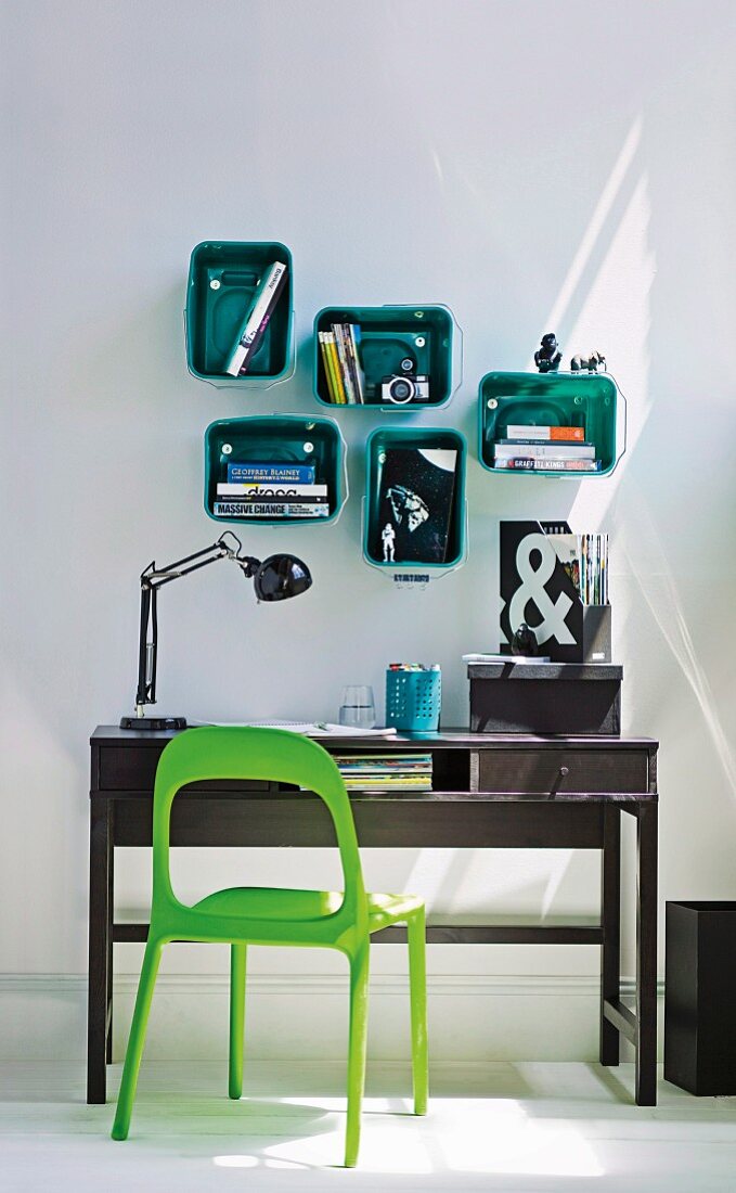 Grass green plastic chair at black wooden bureau and modular, plastic box shelves with rounded corners in emerald green mounted on wall