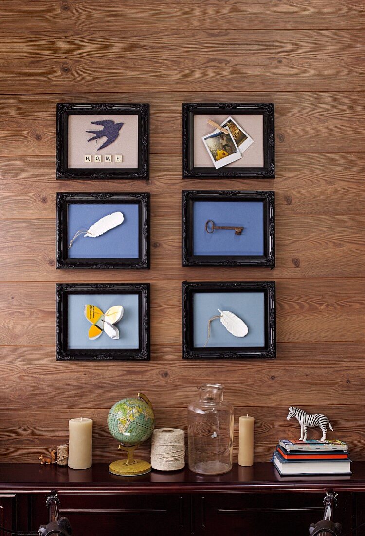Objet d'art in picture frames on wooden wall above various ornaments on sideboard