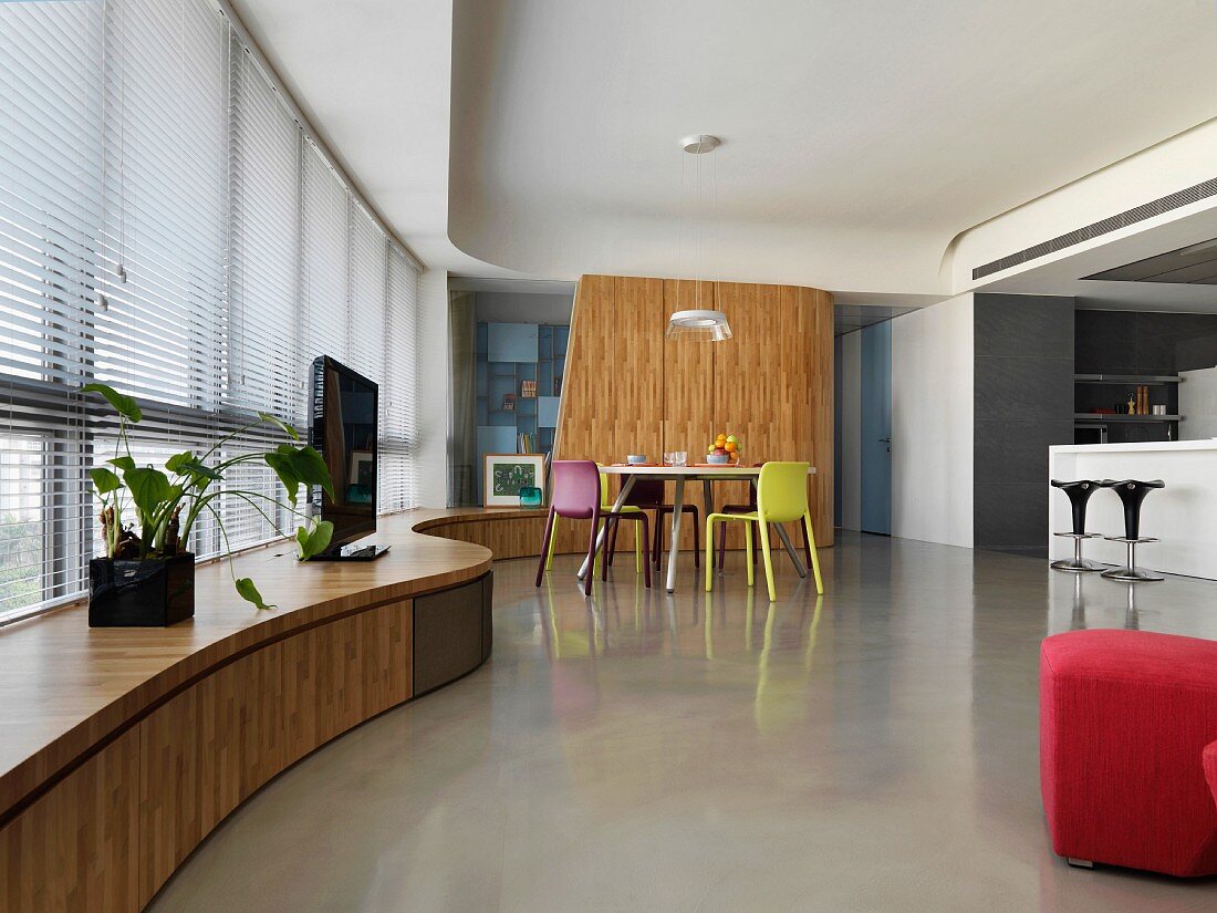 Moderner offener Wohnraum mit geschwungener Fensterbank aus Holz und Essplatz mit farbigen Stühlen
