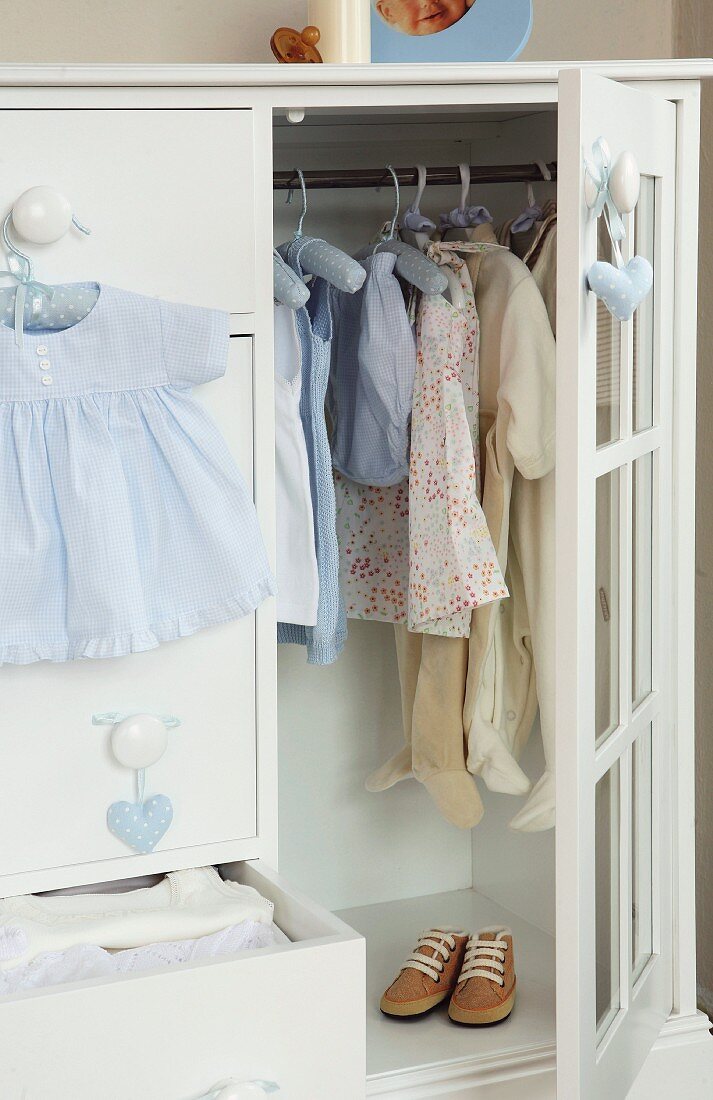 White wardrobe with open door showing child's clothes hanging on rail