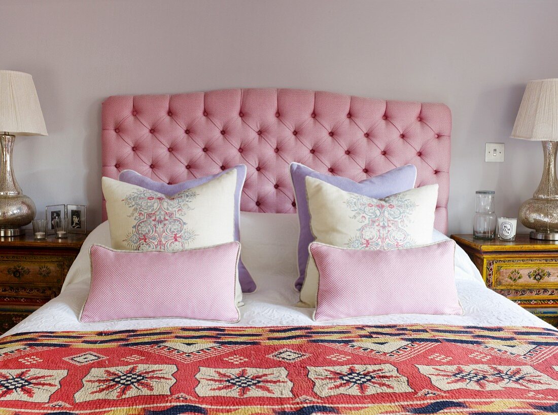 Doppelbett mit drapierten Kissen vor gepolstertem Kopfteil mit rosa Stoffbezug
