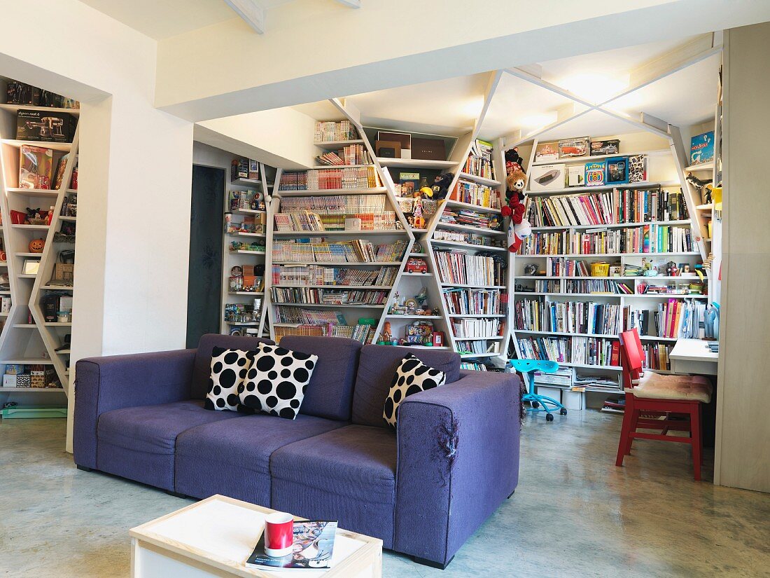 Lila Polstersofa vor raumgreifenden Bücherregalen in modernen Wohnraum