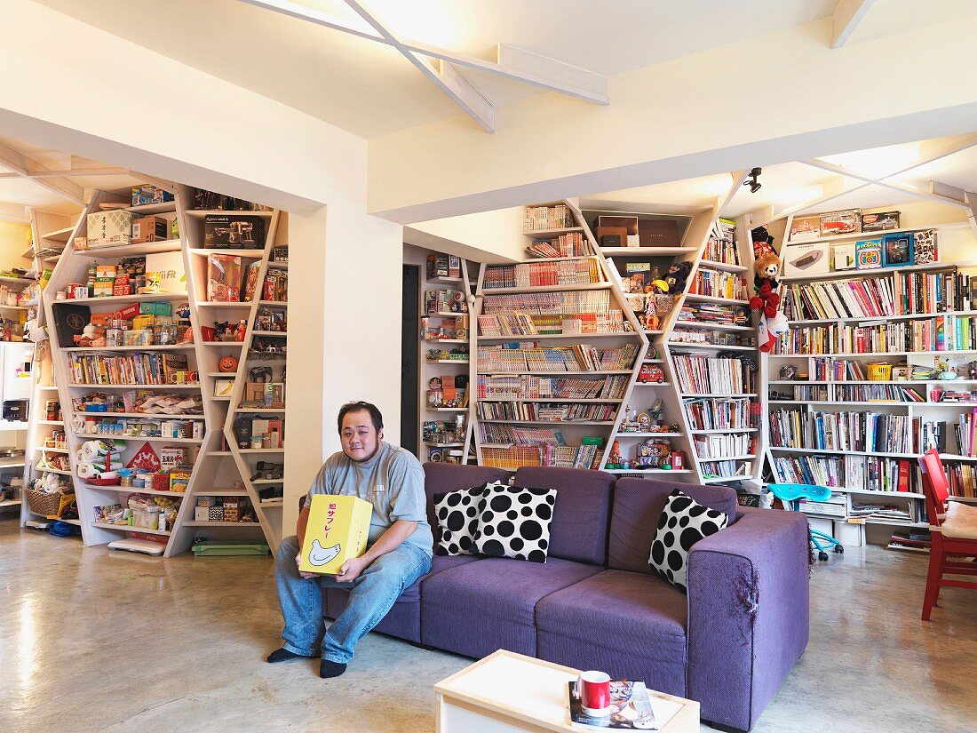 Mann auf lila Sofa vor raumgreifenden Bücherregalen in offenem Wohnraum