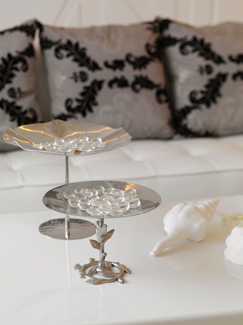 Glass beads on a metal etagere on a white table in front of a sofa with pillows