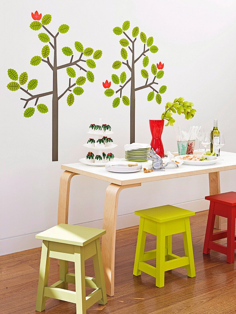 Esstisch mit bunten Sitzhockern vor Wand mit aufgeklebtem Baummotiv