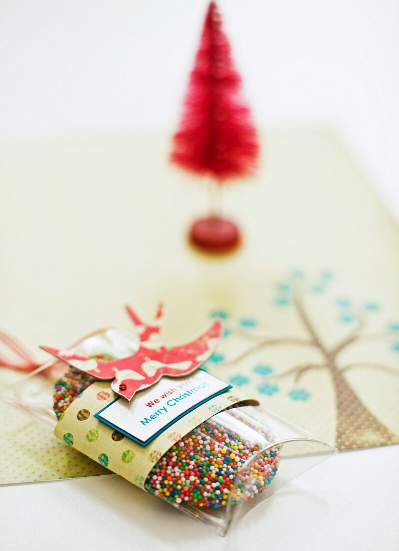 Verpackte Weihnachtsplätzchen mit bunten Zuckerstreuseln und rotes Dekobäumchen im Hintergrund