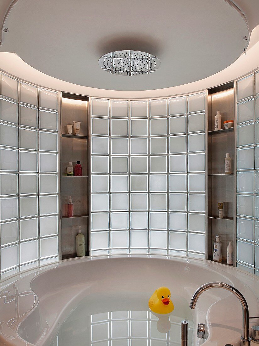 Eine runde Badewannennische mit Glasbausteinwand und Regenwaldduschkopf an der abgehängten Decke
