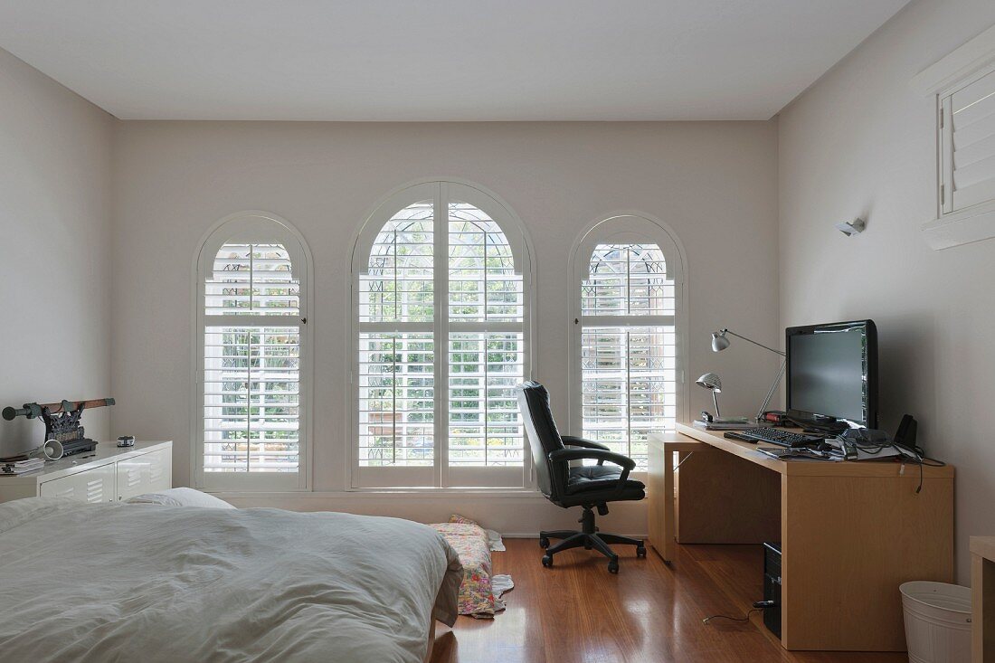 Home office desk with a giant flat screen TV in a bedroom with three arched windows