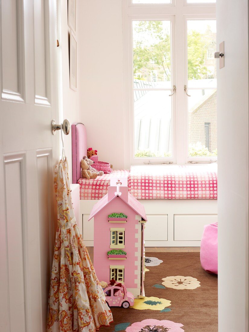Blick durch offene Tür auf Puppenhaus am Boden vor traditionellem Kinderbett am Fenster