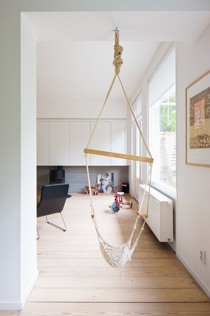Hammock swing in doorway and view into minimalist living room with black armchair and white wall units