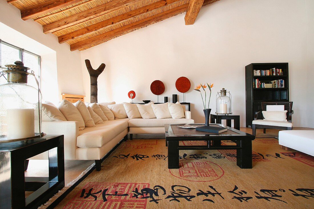 Modernes Ecksofa mit vielen Kissen und schwarzer Hochglanzcouchtisch auf einem großen Asiateppich im Wohnzimmer