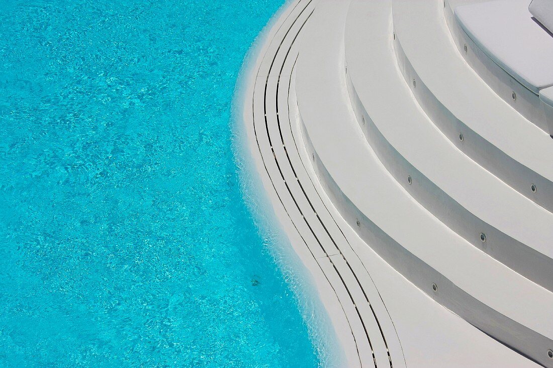 Eine weiße, abgerundete Treppe führt zum Pool mit geschwungenem Rand