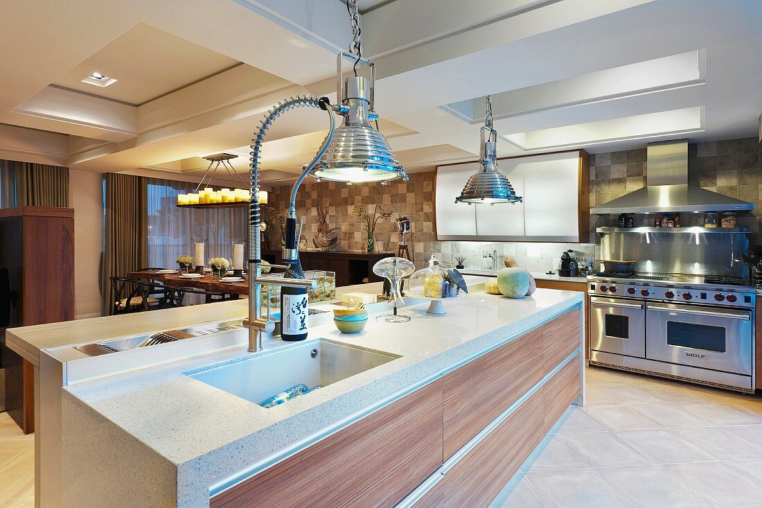 Küchenblock aus Stein und Tropenholz in grosszügiger, moderner Wohnküche mit Oberlichtkassetten und Hängelampen im Industriestil