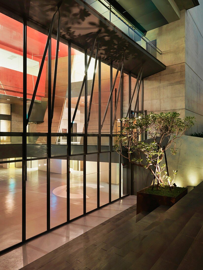 Abendstimmung - Blick von Draussen durch moderne Glasfassade in erleuchtete Lobby mit roter Deckenverkleidung