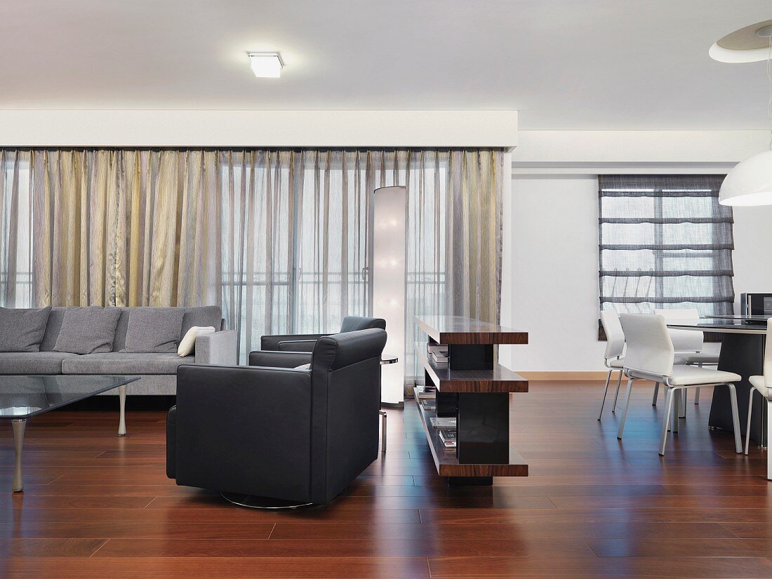 Halbhohes Raumteilerregal zwischen Sitzbereich mit grauen Sofas und rundem Essplatz