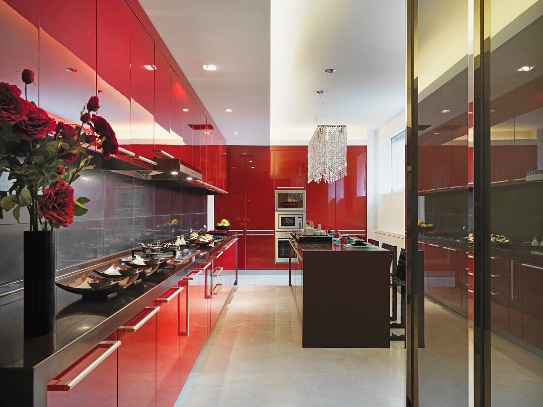 Elegante Einbauküche mit leuchtend roten Fronten und Edelstahlarbeitsfläche im Kontrast zu klassisch elegantem Kronleuchter