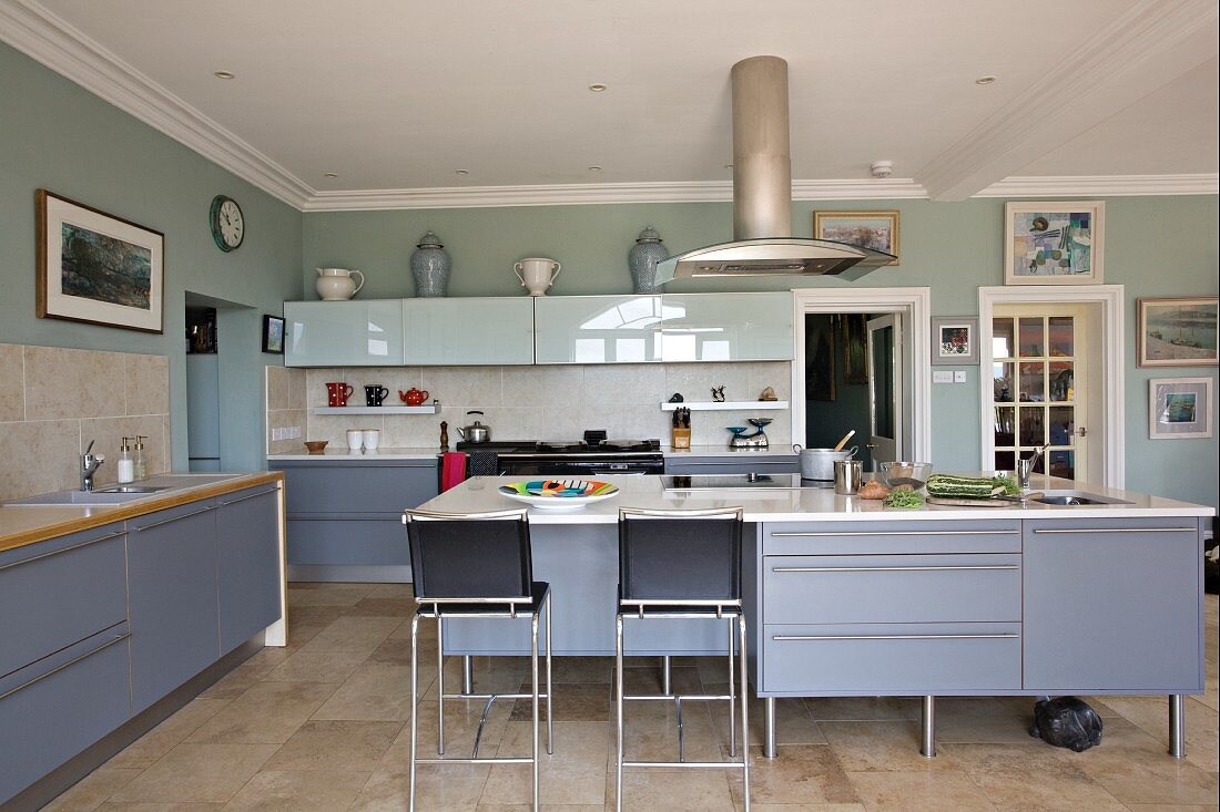 Moderne, große Küche mit blau-grauen Schrankfronten und Barhocker vor freistehendem Küchenblock in ländlichem Ambiente