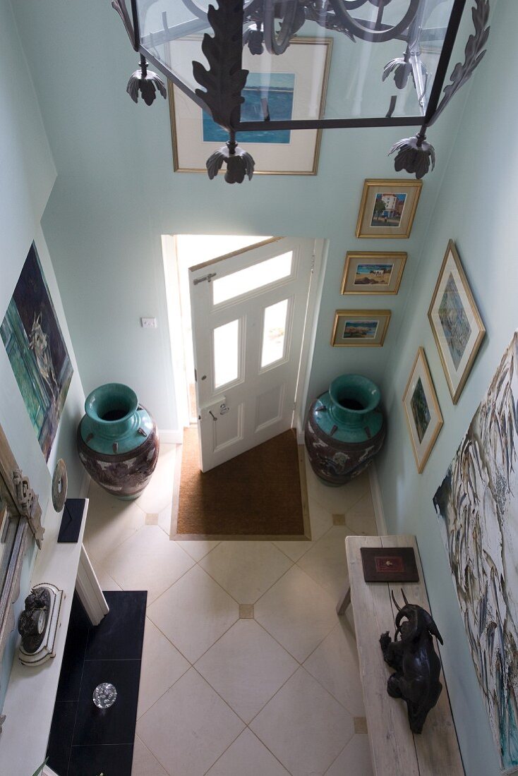Blick von oben auf Bodenvasen und Holzbänke im Hausflur mit diagonal verlegtem Fliesenboden
