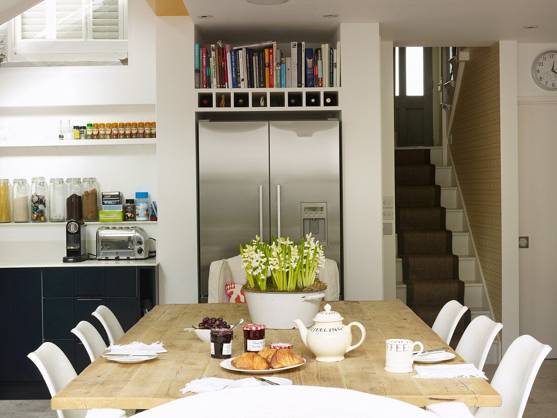 Gedeckter Frühstückstisch in offener Küche mit Kühlschrankkombination aus Edelstahl und Blick auf Treppenaufgang
