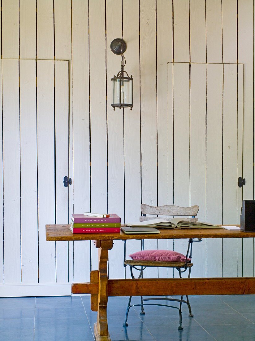 Holztisch mit Büchern und einem Stuhl vor einer holzvertäfelten Wand
