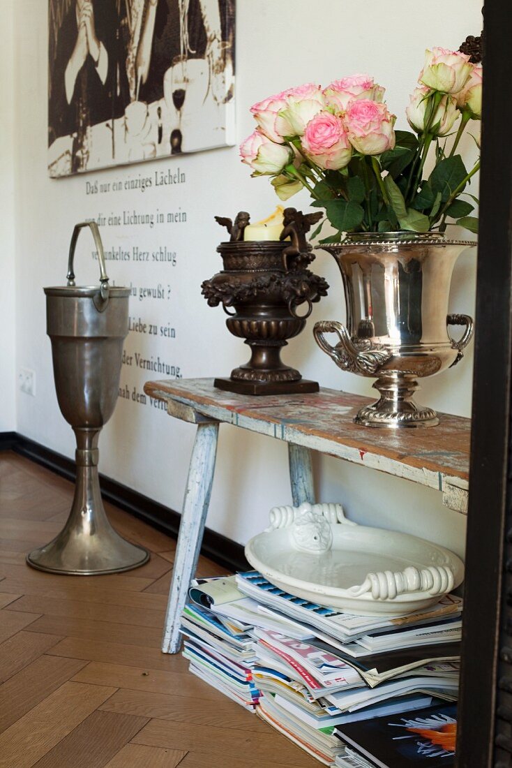 Pokale mit Rosen und Kerze auf einer Holzbank, darunter Zeitschriften und weiße Servierplatte