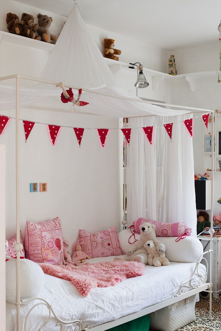 White canopied bed with pink scatter cushions and blanket in girl's bedroom