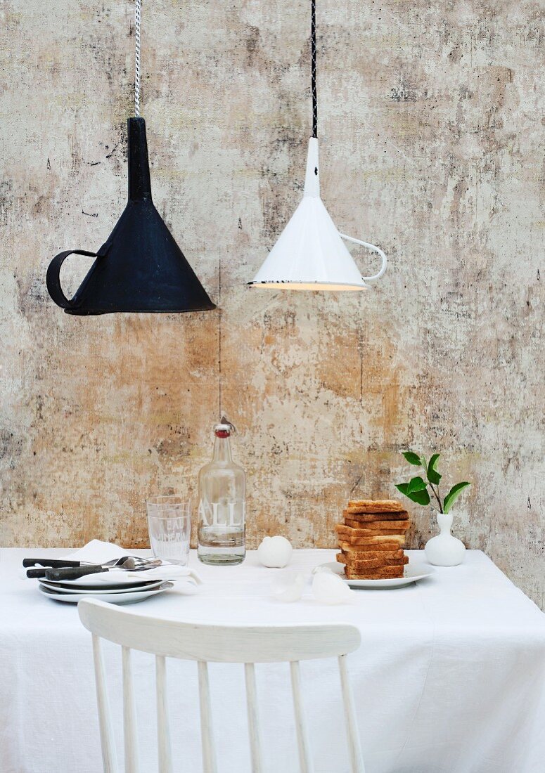 Weisser und schwarzer Trichter als origineller Lampenschirm über Küchentisch mit Toastbrotstapel