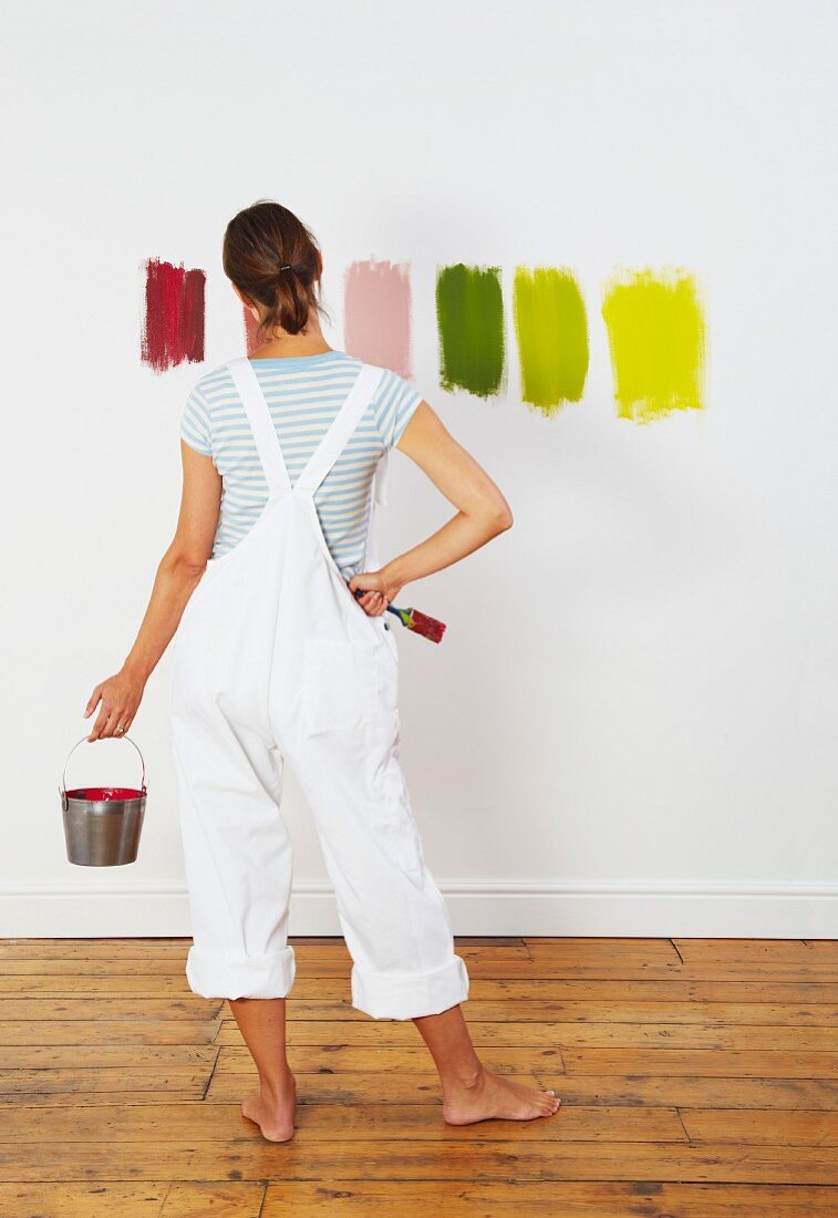 Junge Frau betrachtet verschiedene Farbmuster auf Zimmerwand