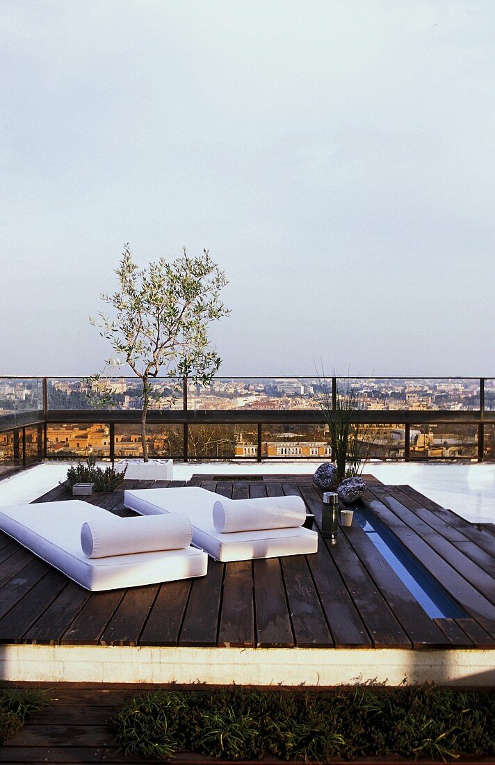 Wooden platform with loungers on a roof terrace with a view across the city