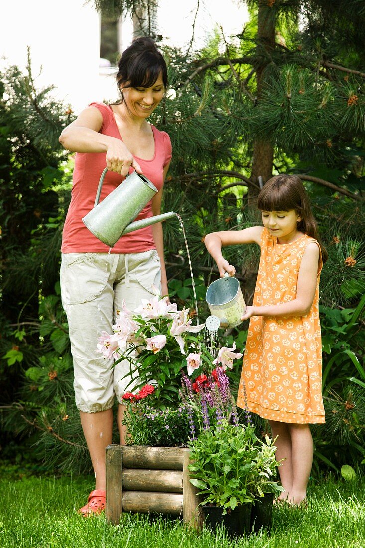 Mutter und Tochter gießen Topfblumen im Garten