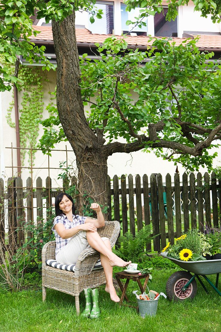 Frau sitzt im Korbstuhl im Garten
