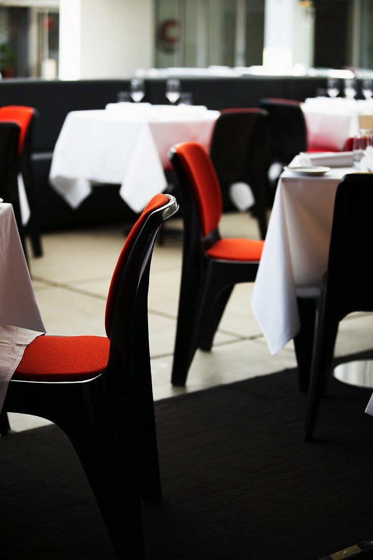 Gedeckte Tische, dazu Stühle mit orangefarbenen Sitzpolstern in einem Restaurant