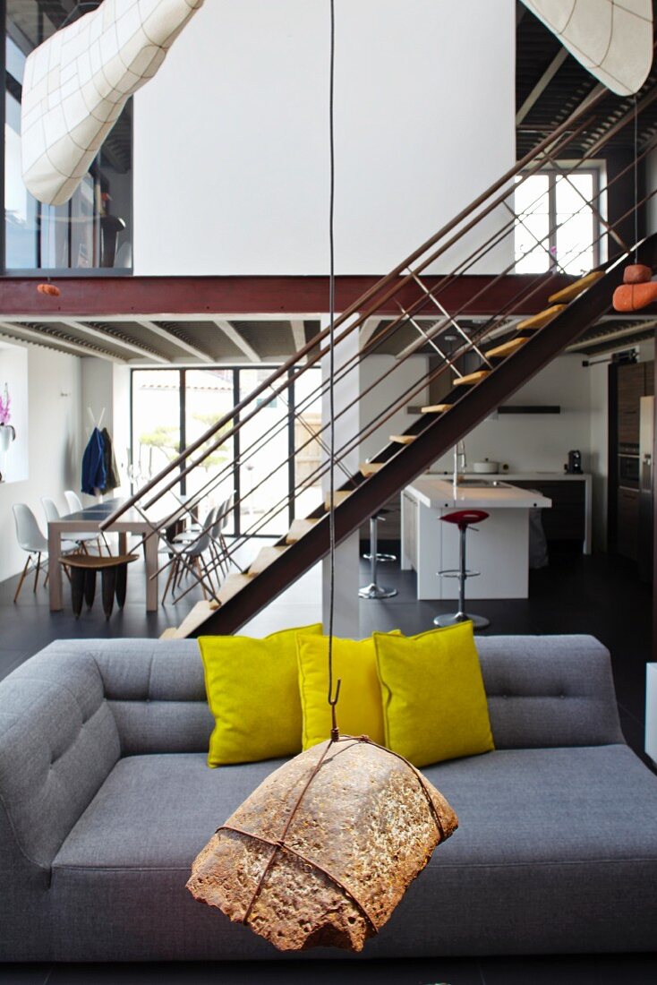 Hängendes Kunstobjekt vor grauem Designersofa mit gelben Kissen in loftartigem Wohnraum