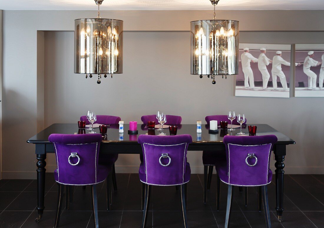 Opulenter Essbereich mit versilberten Hängeleuchten und violetten Samtstühlen an einem gedeckten, schwarzen Antiktisch
