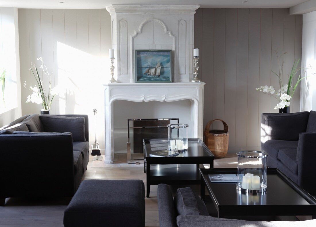 Elegant seating with a black sofa in front of a wooden wall with a classic, white fireplace