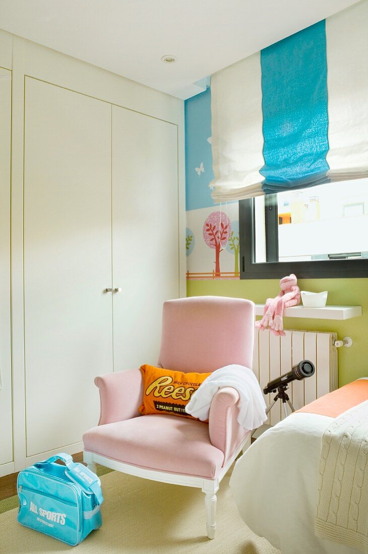 Pastel theme - pink armchair in front of a built in closet and Roman blinds with block stripes in a child's room