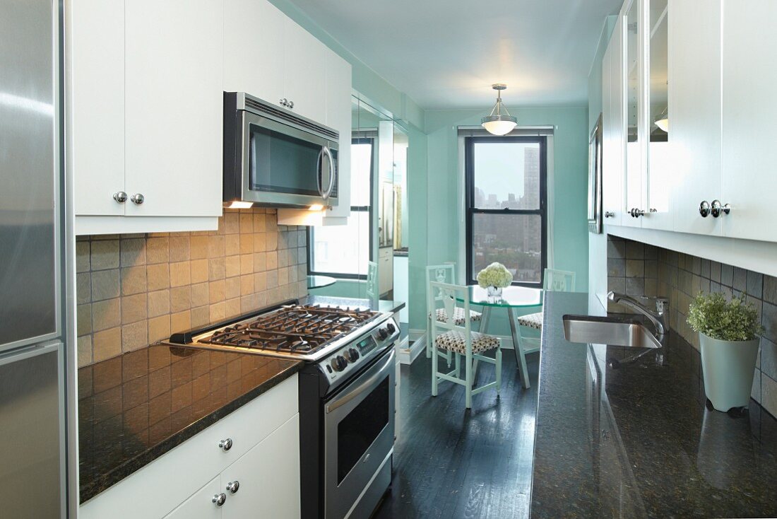 Moderne Einbauküche mit Granitplatten und kleiner Essbereich vor dem Fenster mit Blick auf die New Yorker Skyline