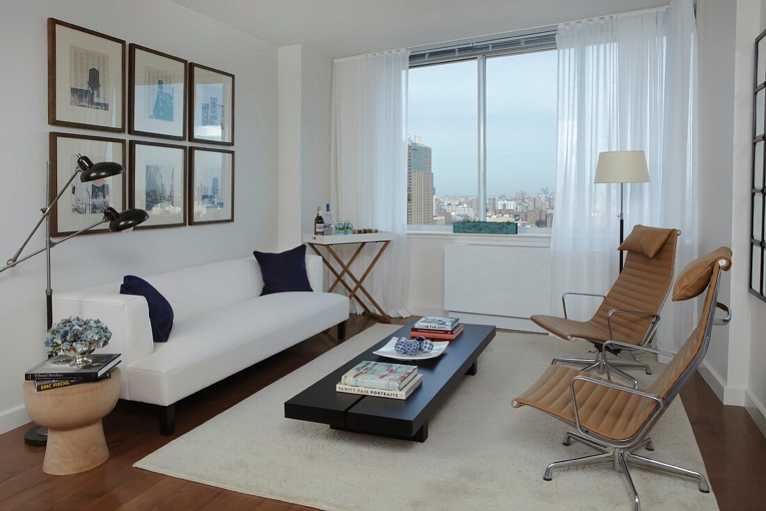 Weisses Polstersofa und elegante Drehsessel im modernen Wohnzimmer mit Blick auf die Skyline