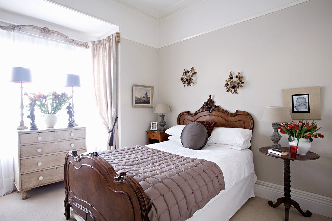 Elegant bedroom; antique bed with bedside table and chest of drawers in window niche