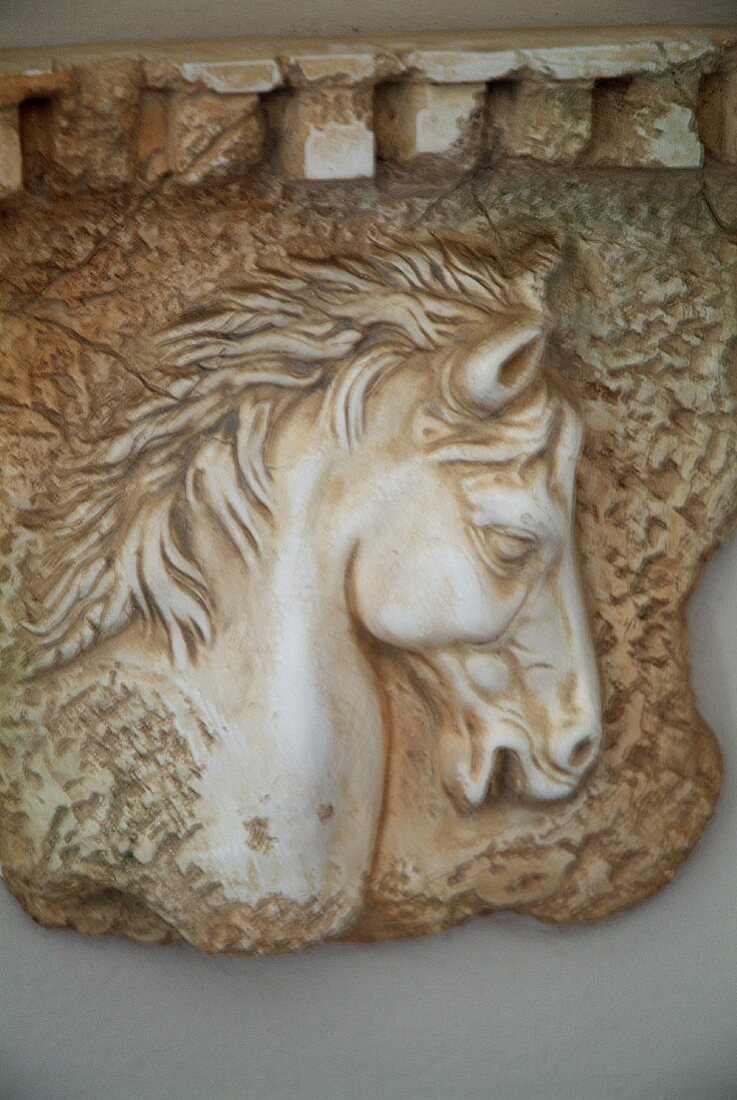 Stone relief of horse head on lilac-painted wall