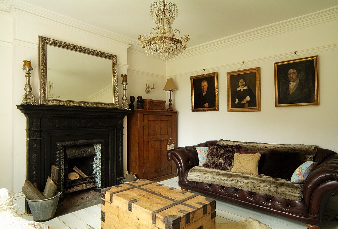 Englisches Herrenzimmer mit offenem Kamin und dunklem Ledersofa, an der Wand Ölgemälde in Goldrahmen; elegant-rustikales Ambiente