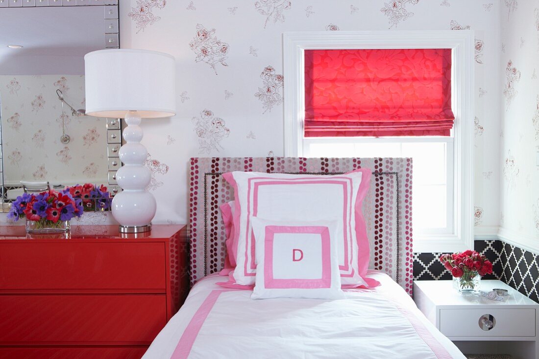 Feminines Schlafzimmer mit gepolstertem Einzelbett vor dem Fenster und roter Schubladenkommode