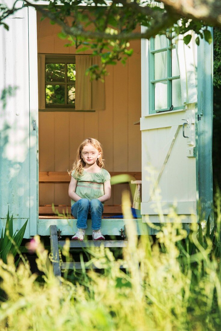 Little girl sitting on the wooden step of a small summer house