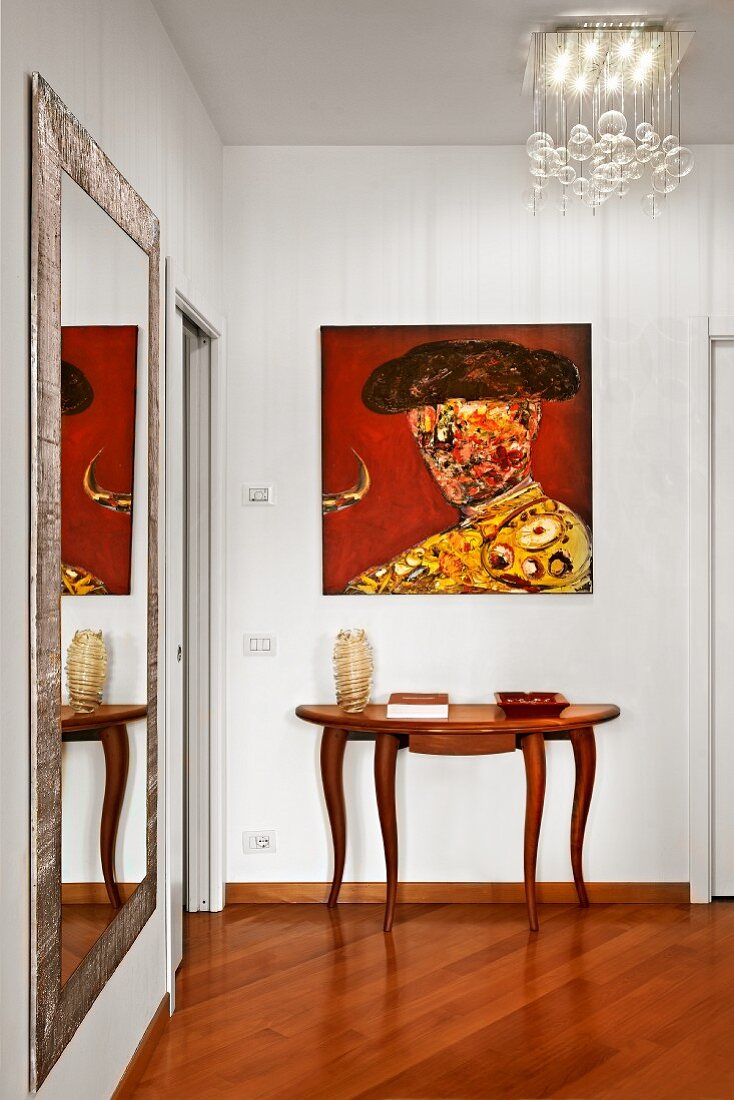 Spanisches Gemälde über einem eleganten Wandtisch im stilgemixten Flur mit Ganzkörperspiegel und Designerlampe