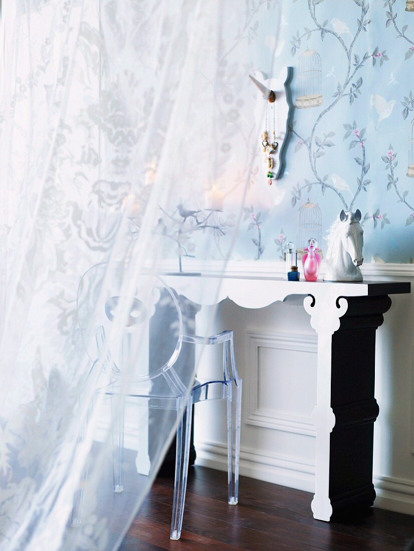 A veiled peek through a half closed voile curtain of a romantic dressing table ensemble in front of floral wallpaper