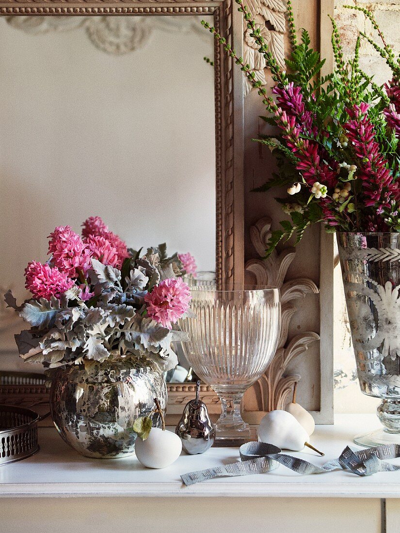 Bouquets in silver-plated vases and crystal goblet on shelf in front of mirror in elegant atmosphere